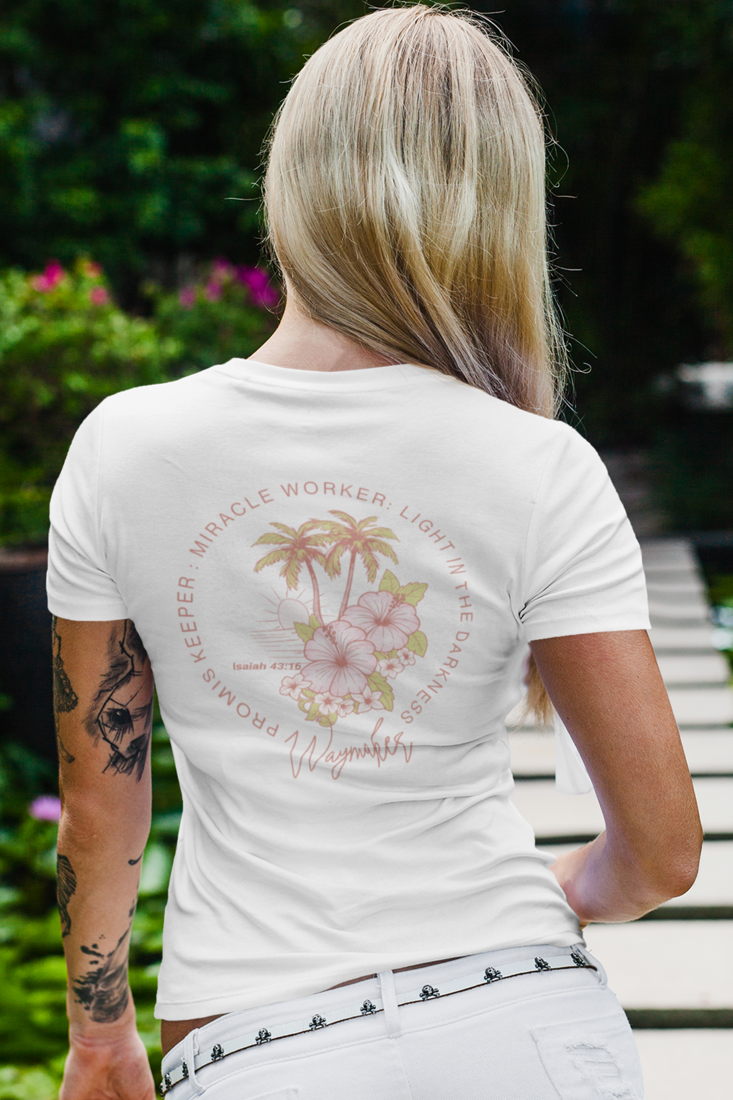 Person wearing a white t-shirt with a floral design and text on the back, standing outdoors.