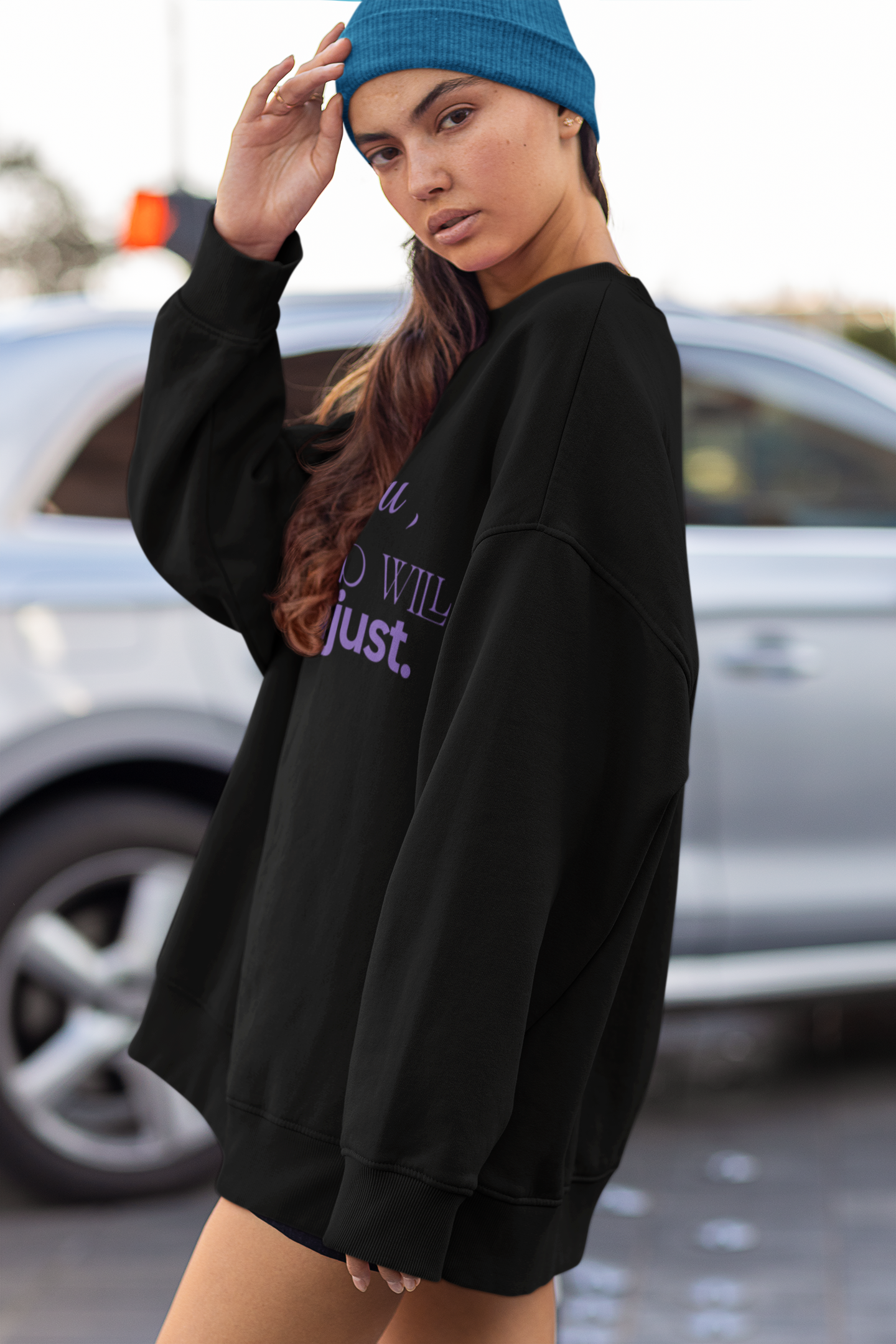 Person wearing a black oversized sweatshirt with text and a blue beanie in an outdoor setting.