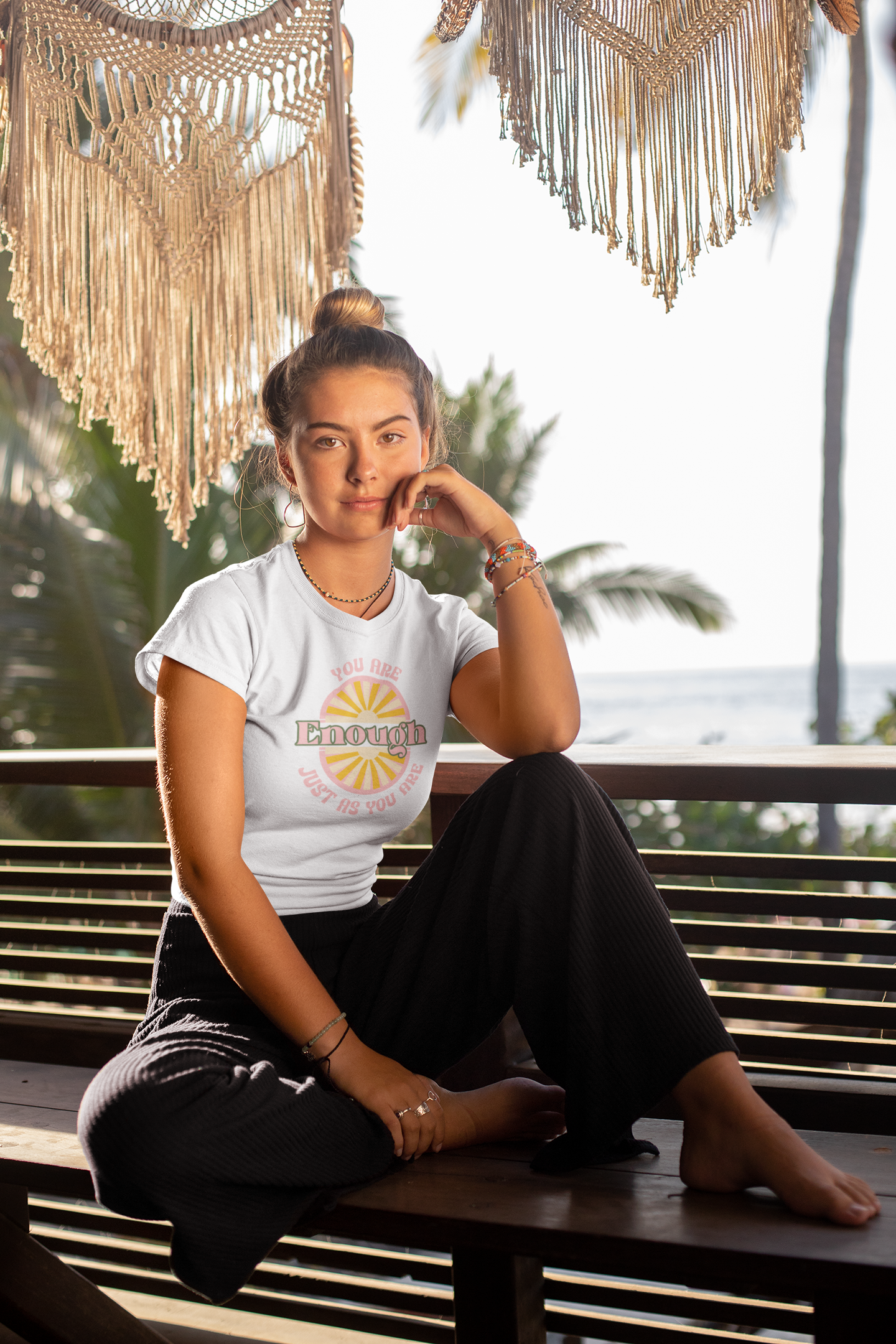 Person wearing a white t-shirt with a graphic design, sitting on a bench with a scenic background.