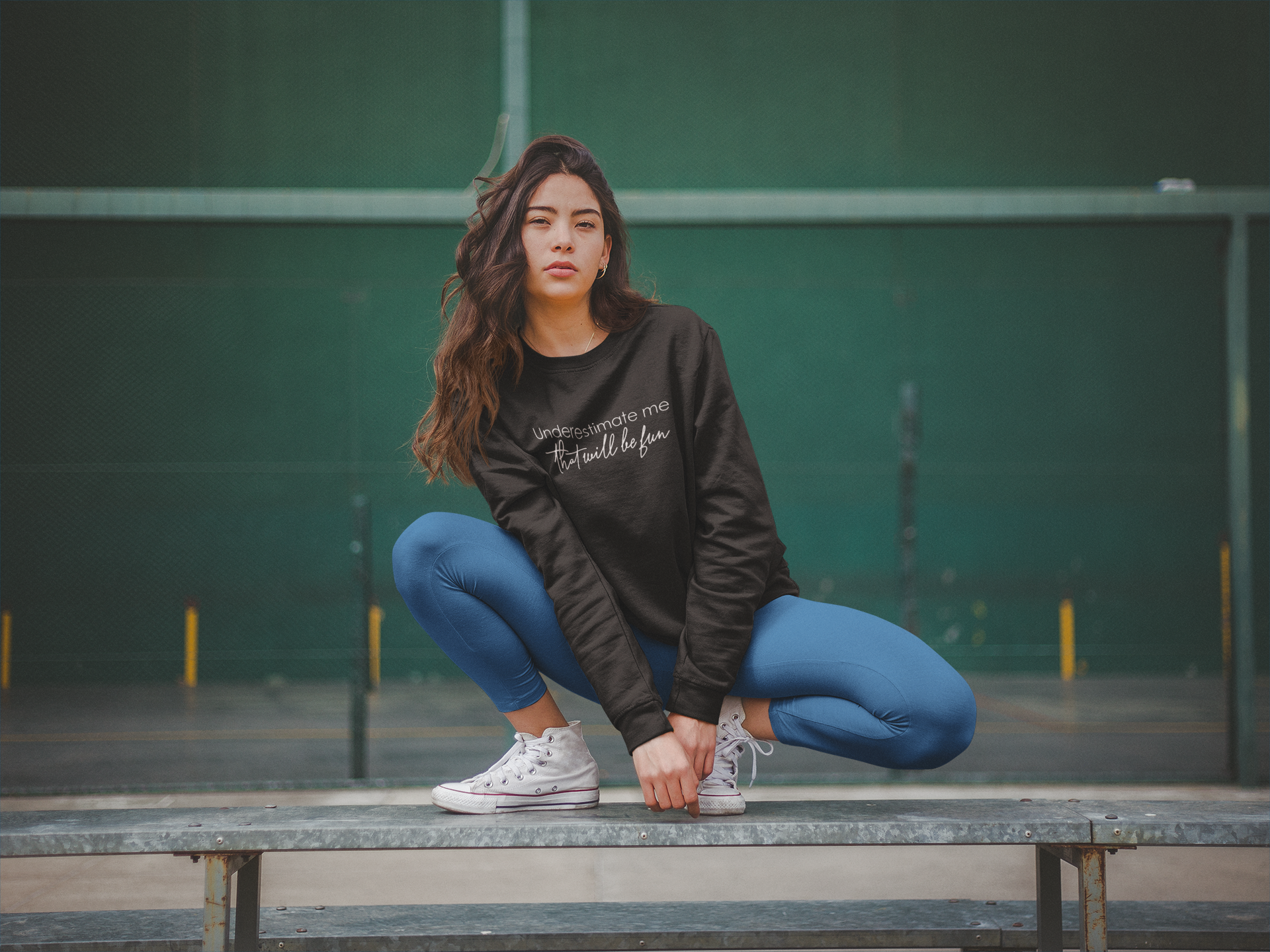 Woman squatting on a bench wearing a black sweatshirt and blue leggings.